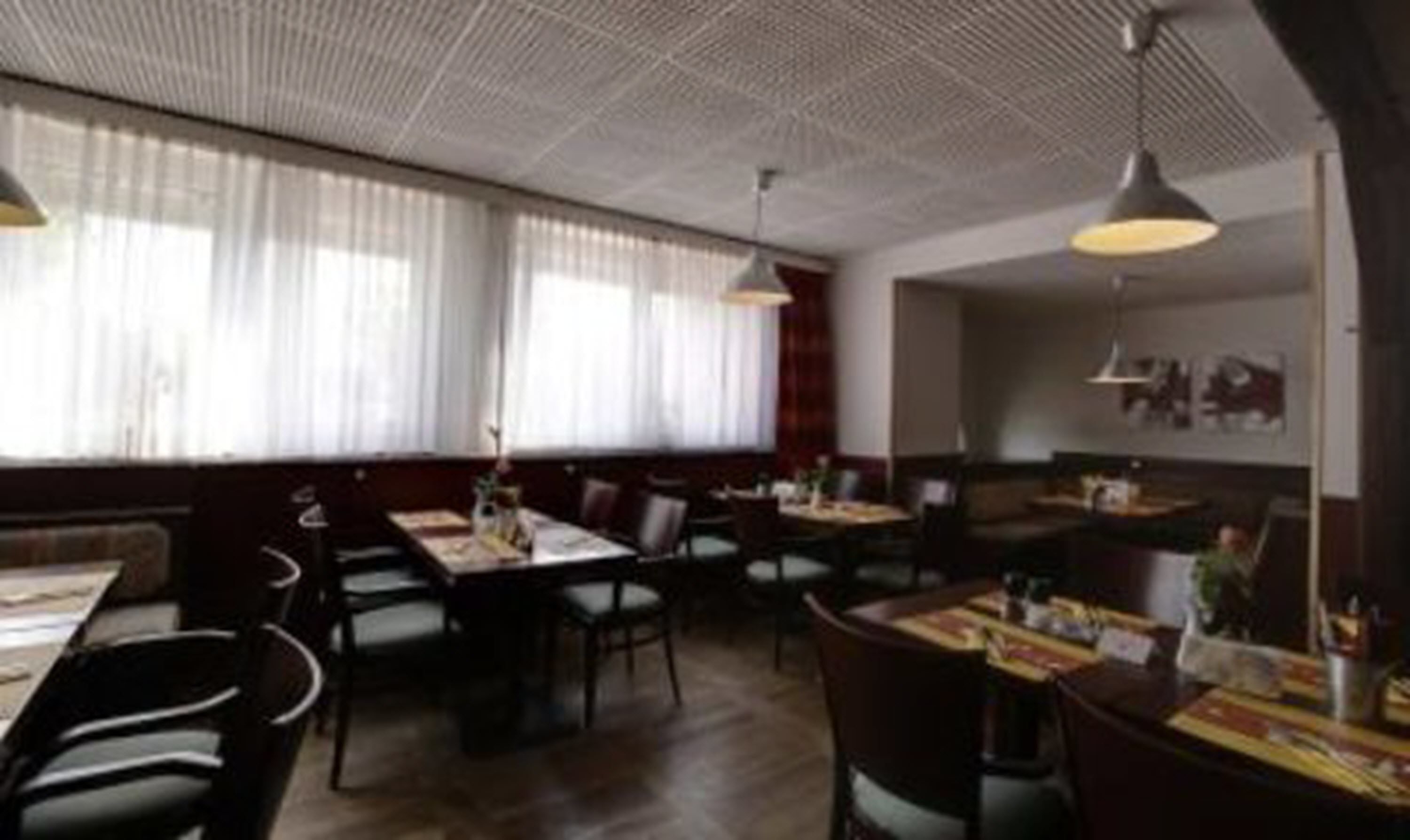 Un restaurante con techos altos, ventanas amplias con cortinas translúcidas y varias mesas y sillas.