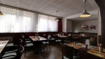 Un restaurante con techos altos, ventanas amplias con cortinas translúcidas y varias mesas y sillas.