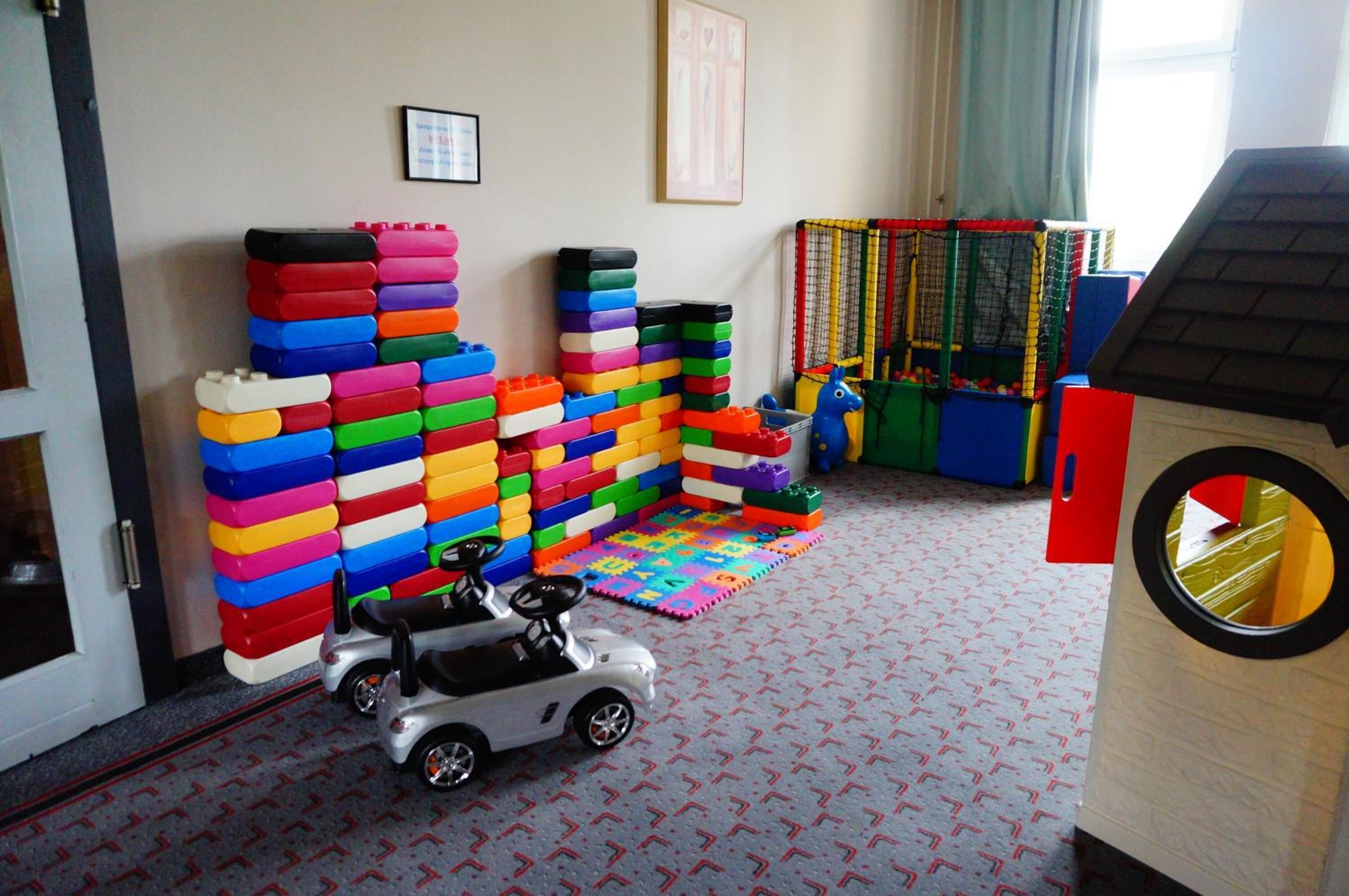A play area with colorful building blocks, a toy car, and a playpen with a ball pit.