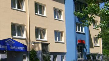 A building with a blue and beige facade, a parked vintage car, and a sign for a restaurant.