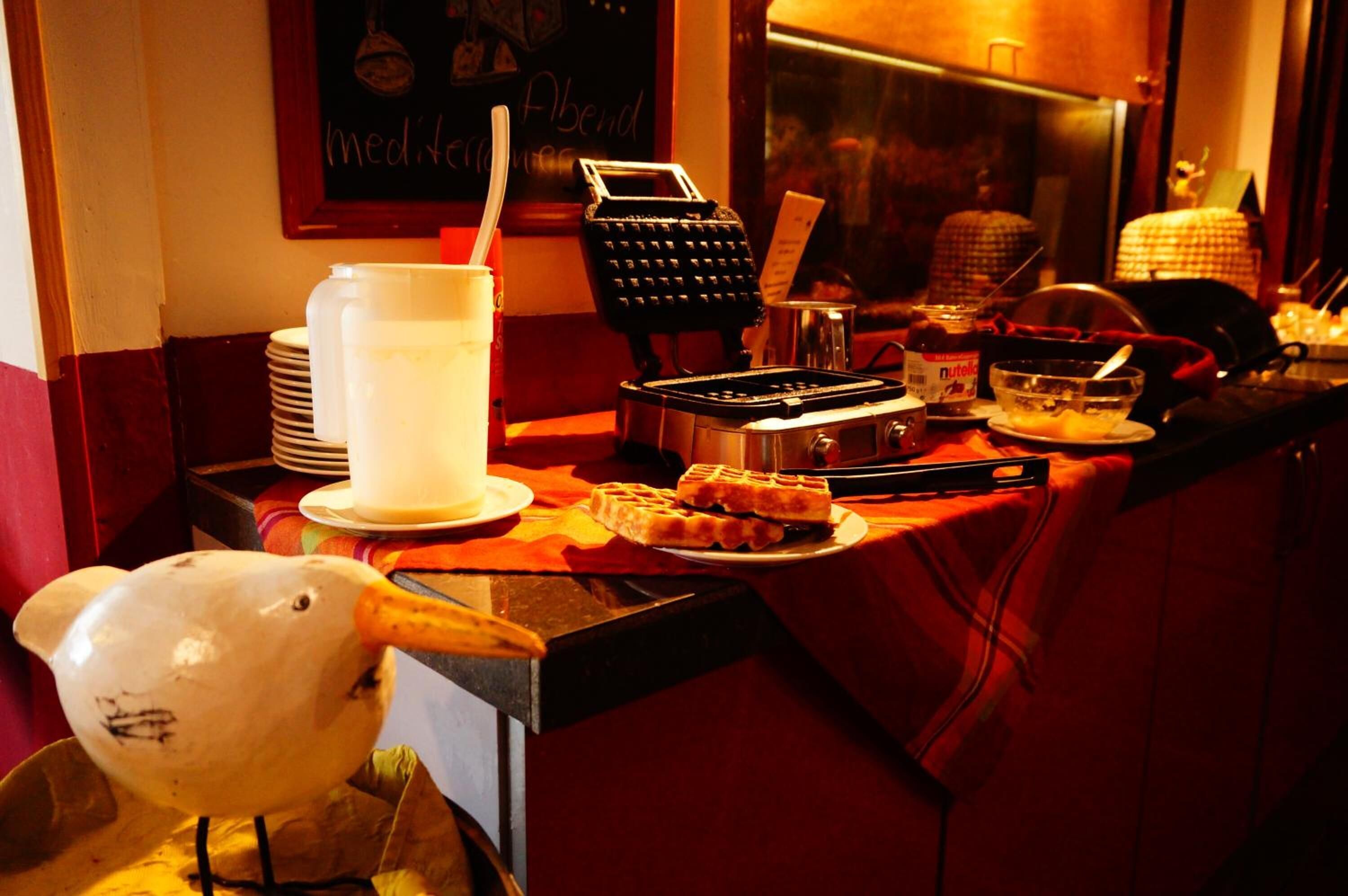 A restaurant counter with a waffle iron, a waffle, a large pitcher, and a waffle server.