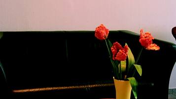En stue med et tulipanmaleri, en gul vase med blomster og et rundt orange bord med en gul og hvid ternet dug.