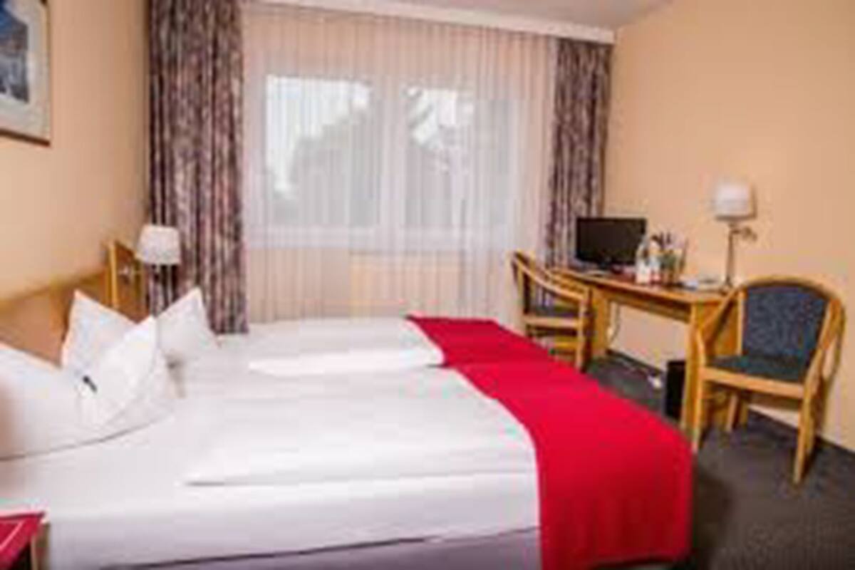 A hotel room with two beds, a desk, a chair, and a television.