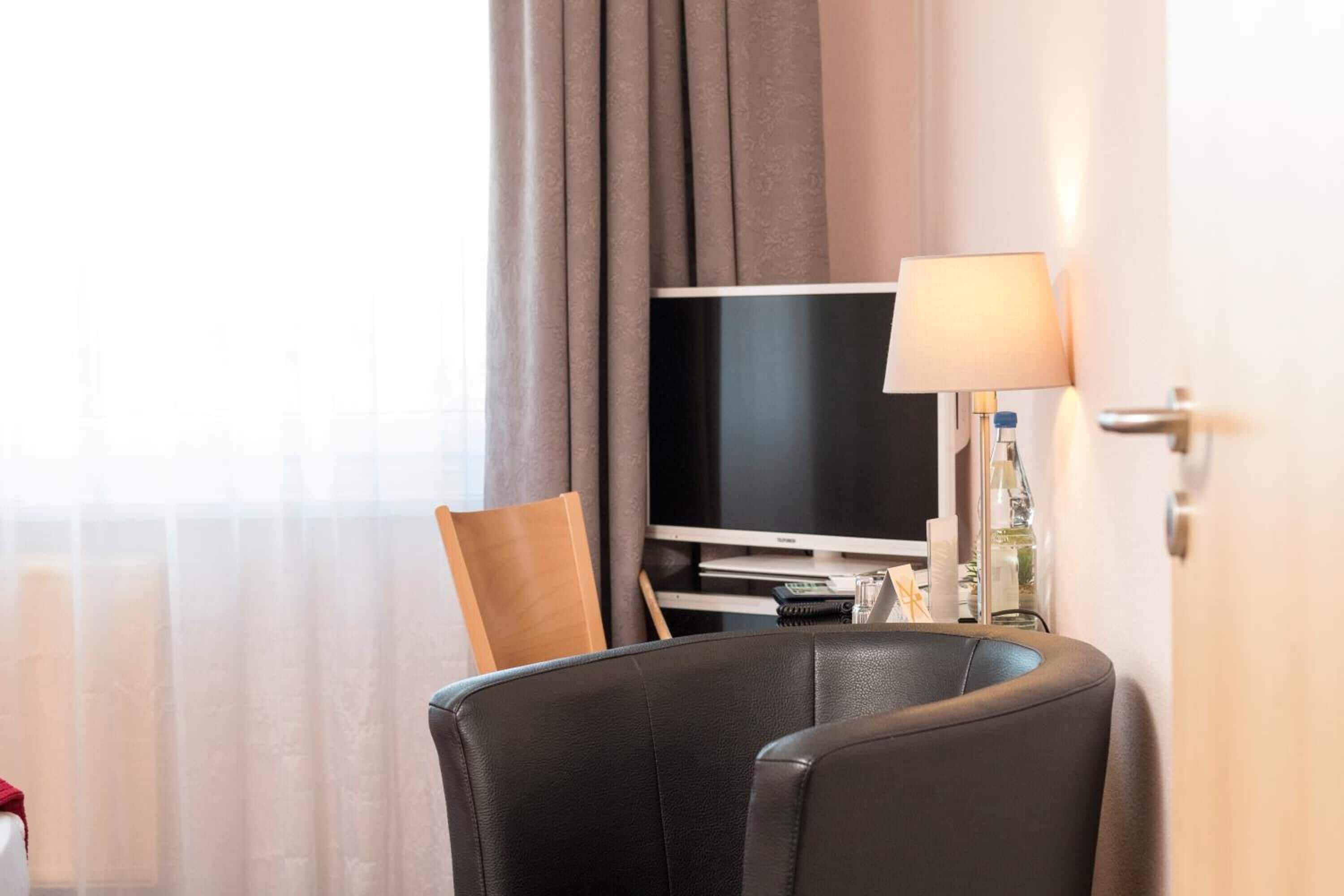 A hotel room with a flat-screen TV, a lamp, and a chair.