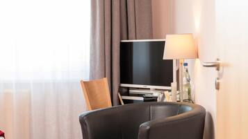 A hotel room with a flat-screen TV, a lamp, and a chair.
