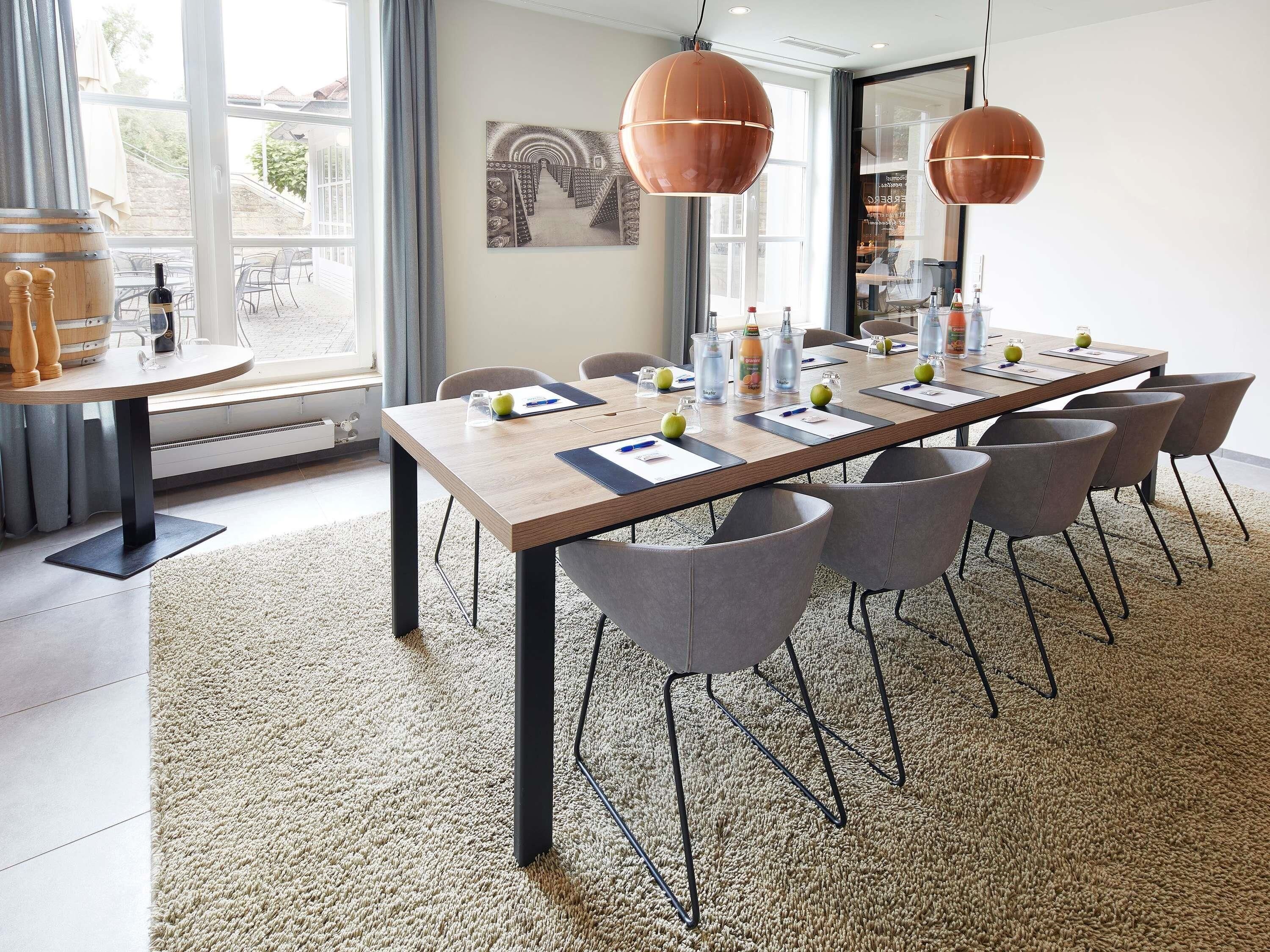 A modern conference room with a long table, grey chairs, and copper pendant lights.