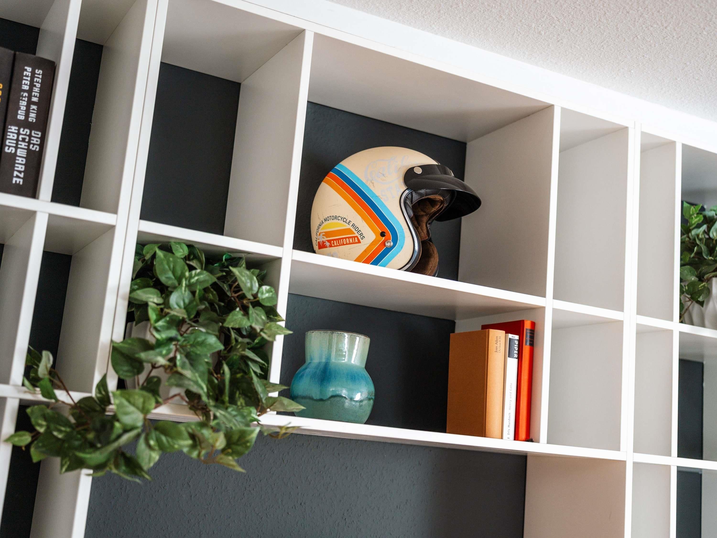 Una estantería con libros, un casco de motocicleta y un florero.