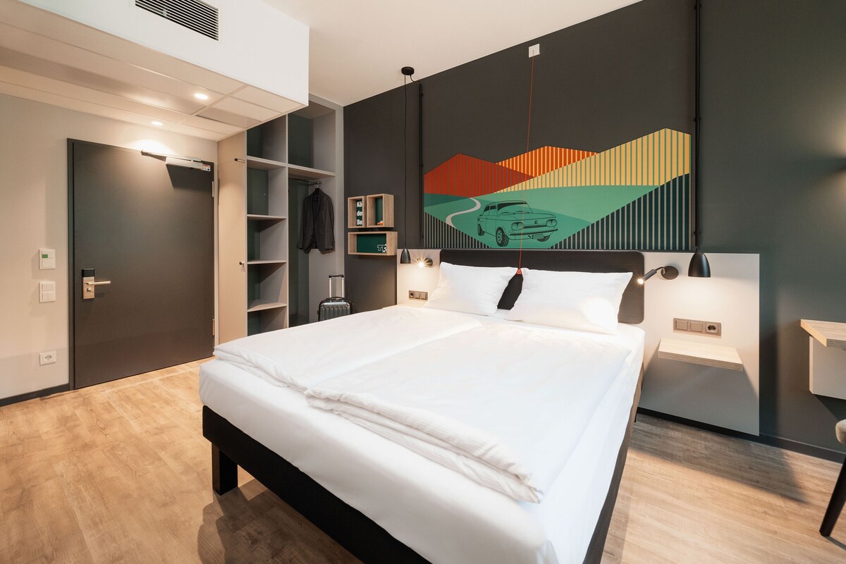 A modern hotel room with a large bed, built-in wardrobe, and a unique wall art piece.
