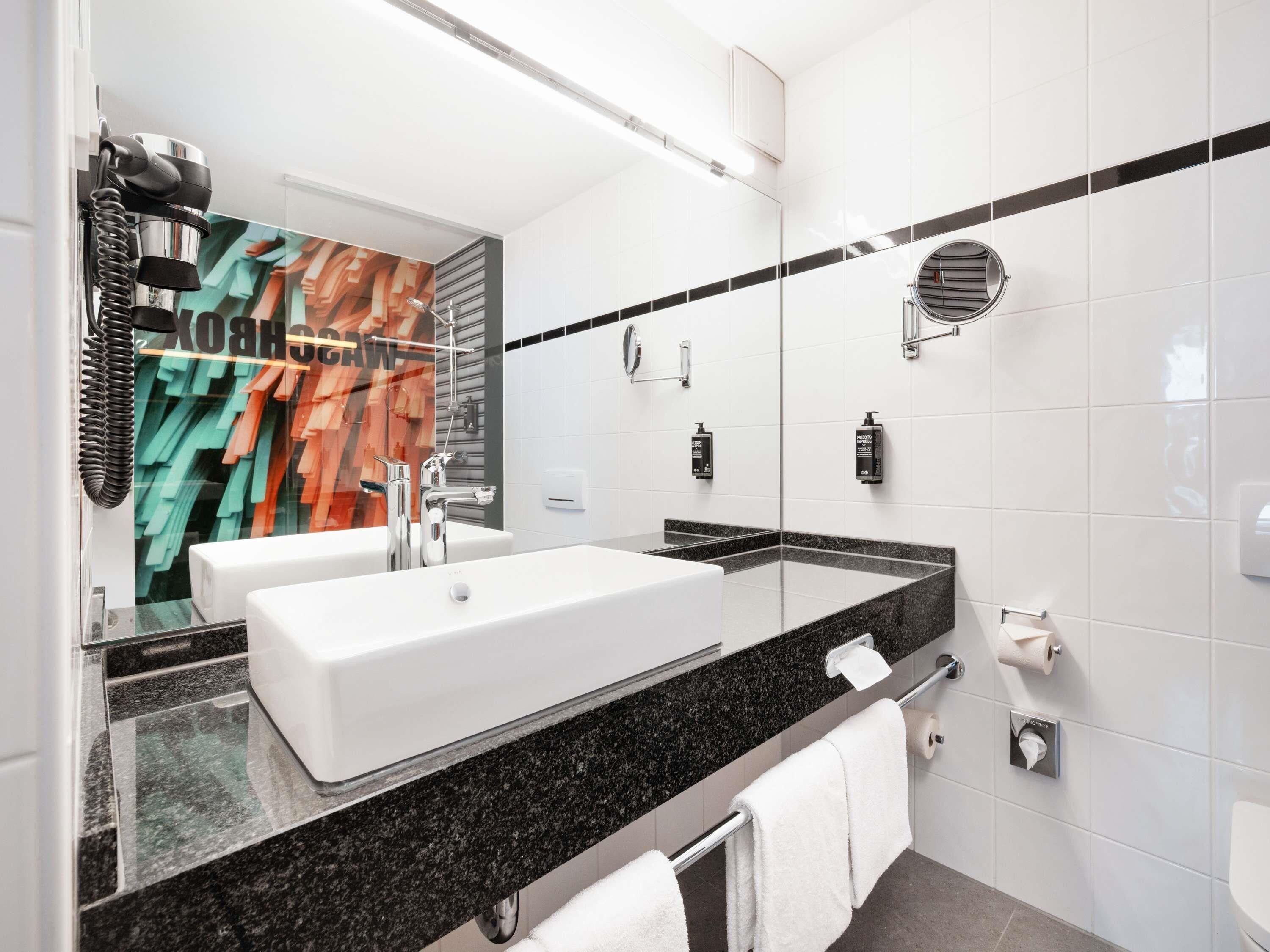A modern bathroom with a large mirror, two sinks, a shower, and a towel rack.