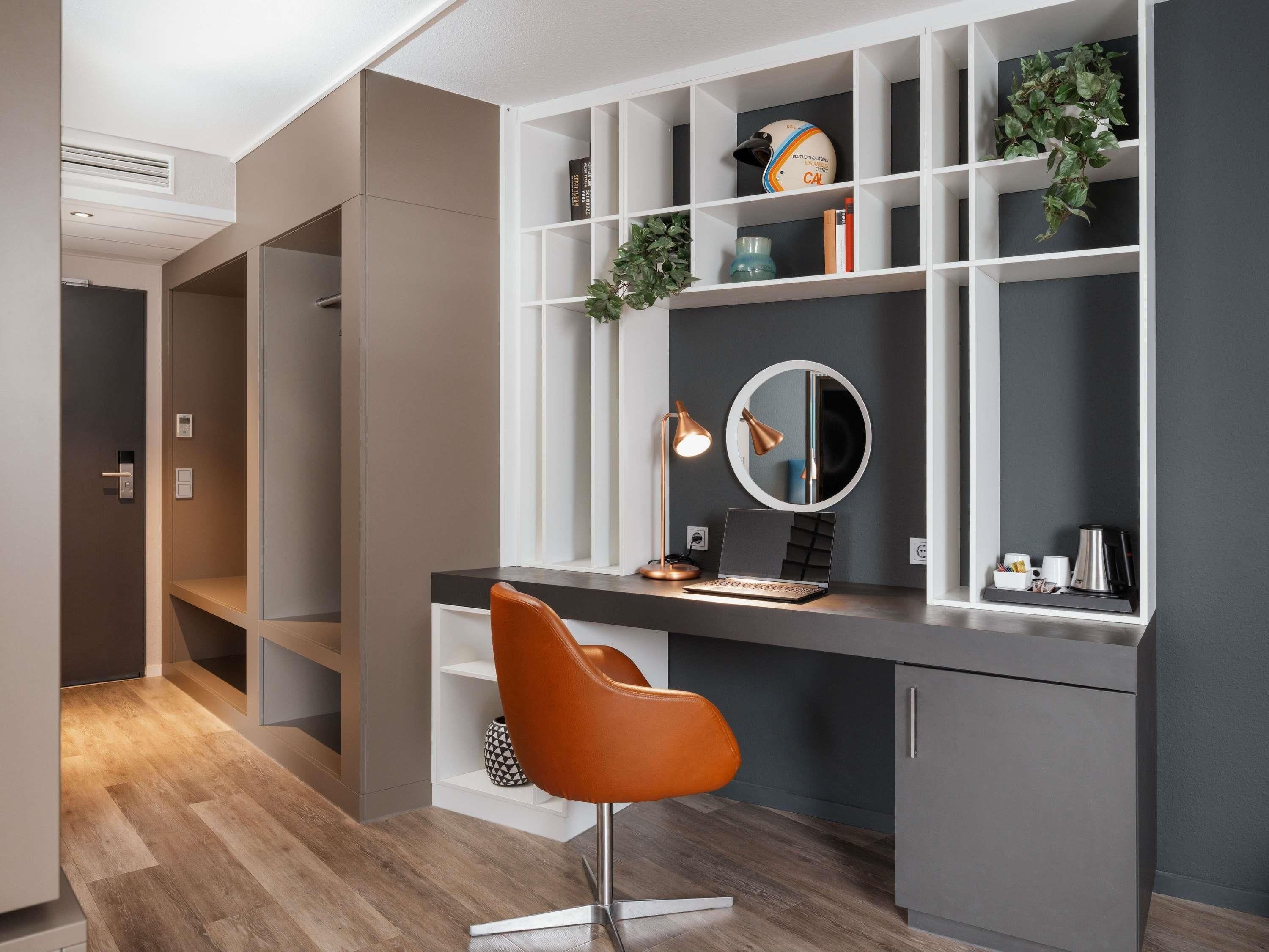 Een moderne kantoorruimte met een bureau, stoel, planken en een spiegel.