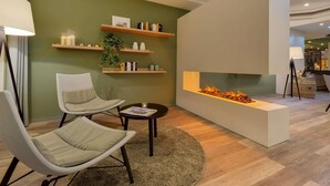 A modern living room with two white chairs, a round coffee table, a fireplace, and wooden shelves with decorative items. - ibis Styles Neckarsulm  (Neckarsulm)