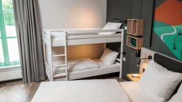 Uma cama beliche com escrivaninha e cadeira, mesa de cabeceira com abajur, janela com cortinas e parede com pintura geométrica.