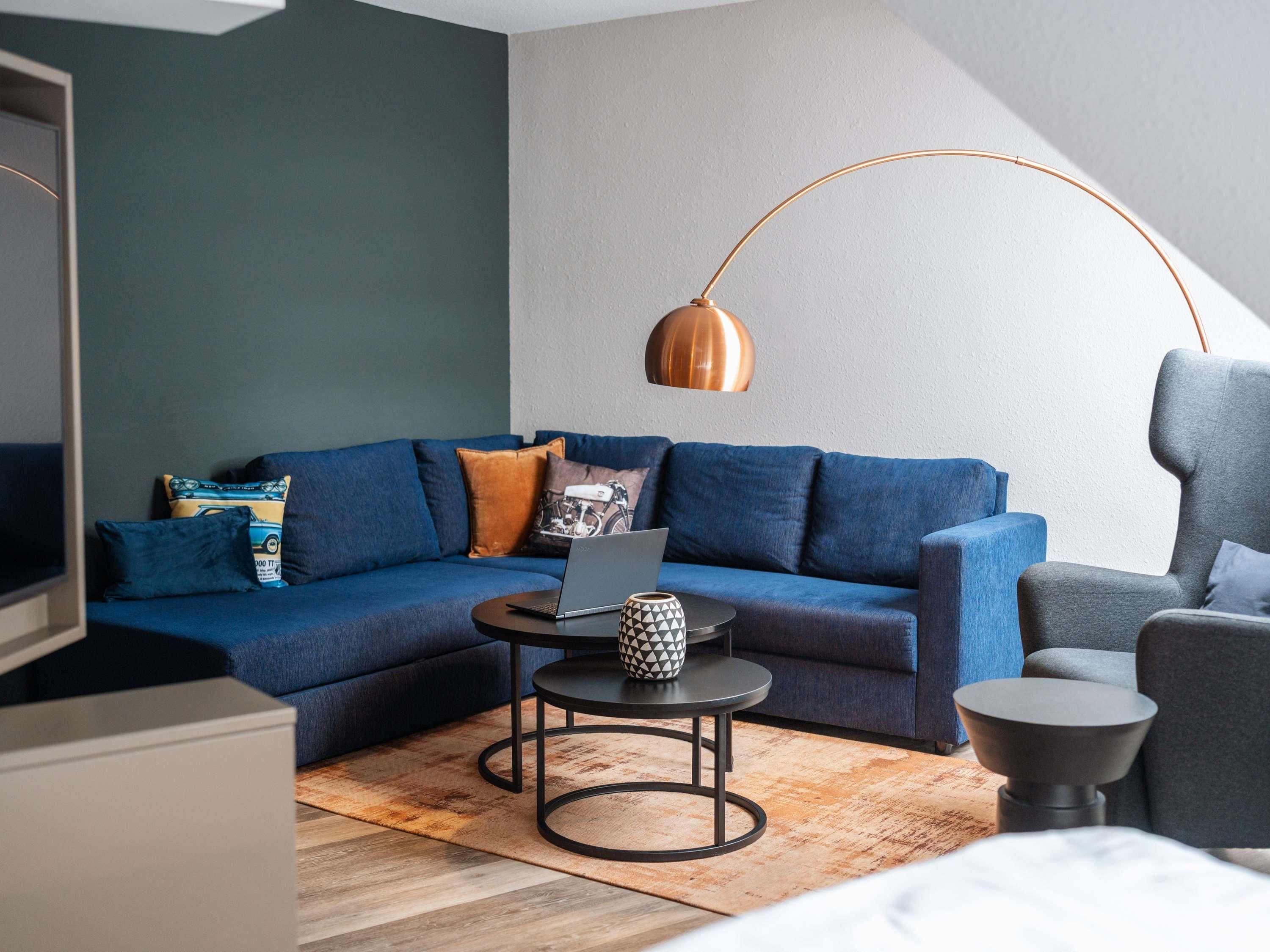 Un salon moderne avec un canapé bleu, un ordinateur portable posé sur une petite table et une lampe originale.
