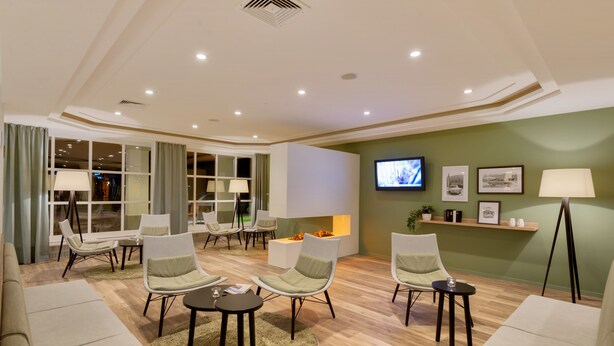A modern living room with a sofa, armchairs, a coffee table, and a TV mounted on the wall. - ibis Styles Neckarsulm  (Neckarsulm)
