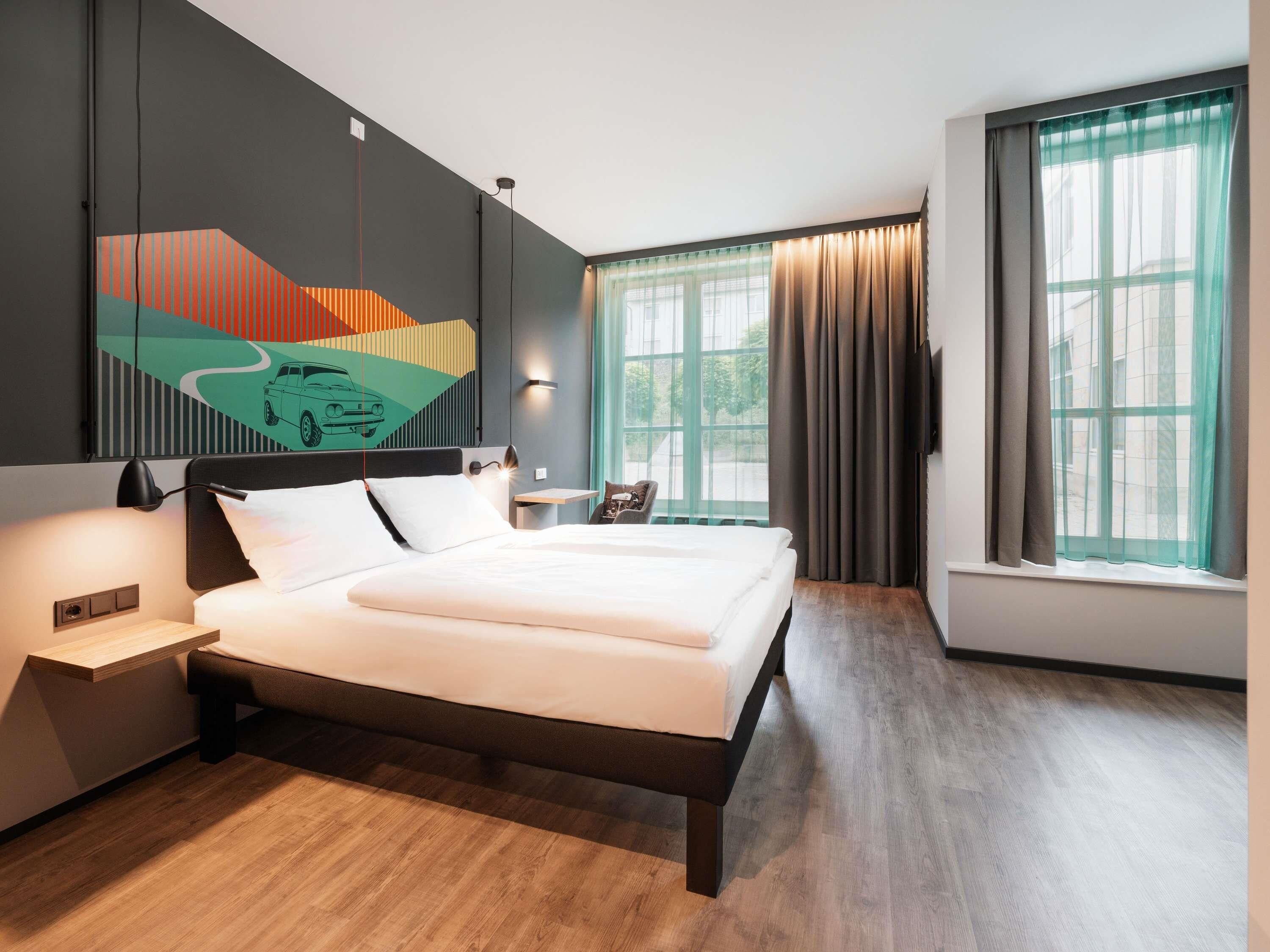 Een moderne hotelkamer met een groot bed, een nachtkastje, een bureau en een raam met gordijnen.