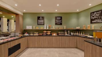 Zona de desayuno tipo bufé con diversas opciones de comida y un letrero que indica servicio para desayuno, almuerzo y cena.