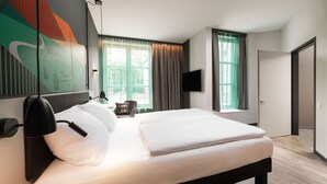 A modern hotel room with a large bed, a flat-screen TV mounted on the wall, and a window with curtains. - ibis Styles Neckarsulm  (Neckarsulm)