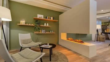 Ein modernes Wohnzimmer mit zwei weißen Sesseln, einem runden Couchtisch, einem Kamin und Holzregalen mit Dekorationselementen.