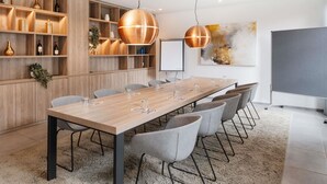 A conference room with a long table, grey chairs, wooden shelving, and two pendant lights. - ibis Styles Neckarsulm  (Neckarsulm)