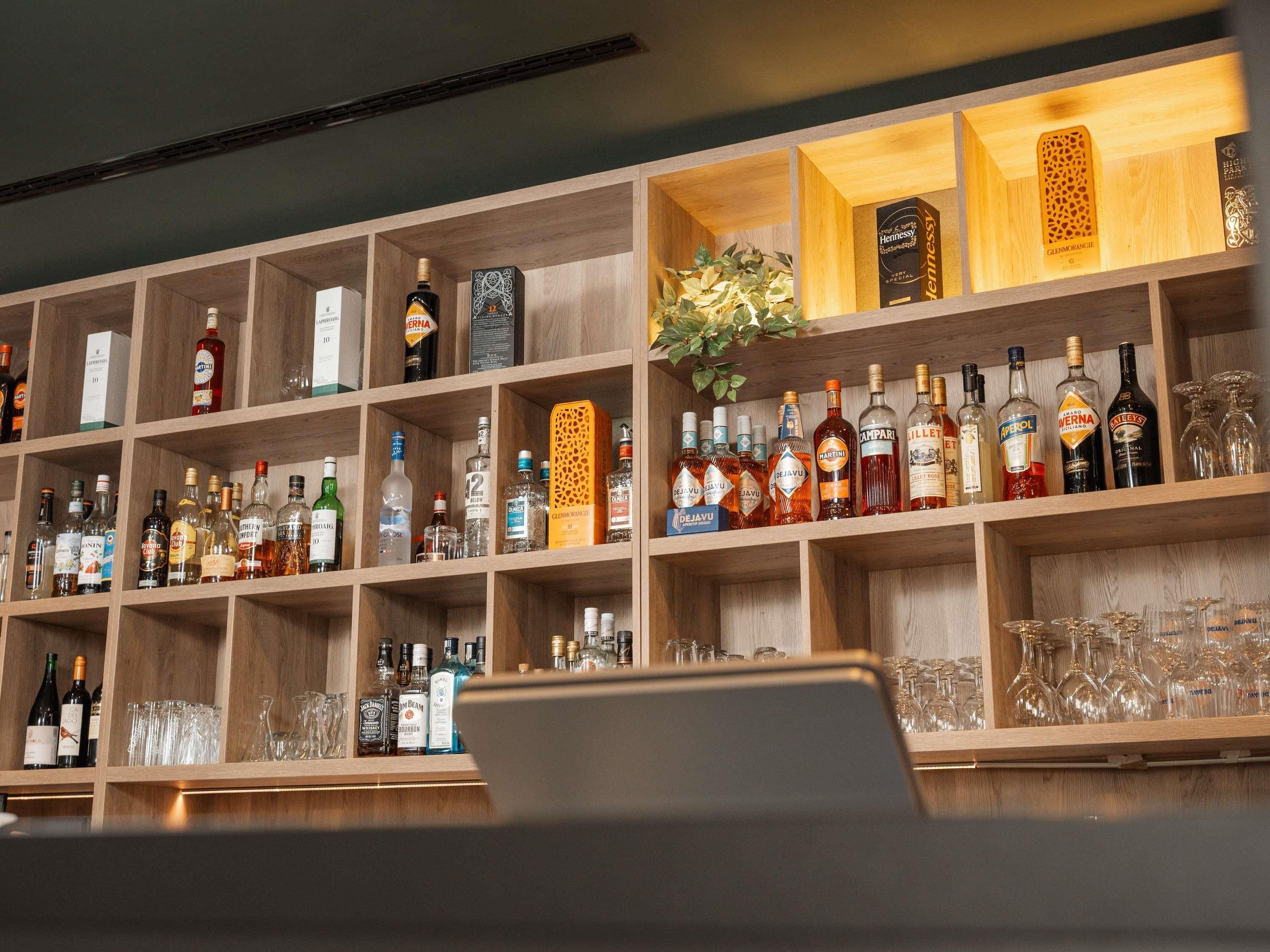 Zona de bar con estantes llenos de botellas de licores y vasos.