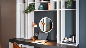 Un espacio de trabajo moderno con escritorio, ordenador portátil, espejo y estanterías con libros y objetos decorativos.