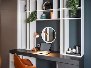 A modern workspace with a desk, laptop, mirror, and shelves with books and decorative items. - ibis Styles Neckarsulm  (Neckarsulm)