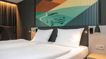 Quarto de hotel com uma cama grande, duas mesas de cabeceira, cabeceira com ilustração de carro e uma luminária fixada na parede.