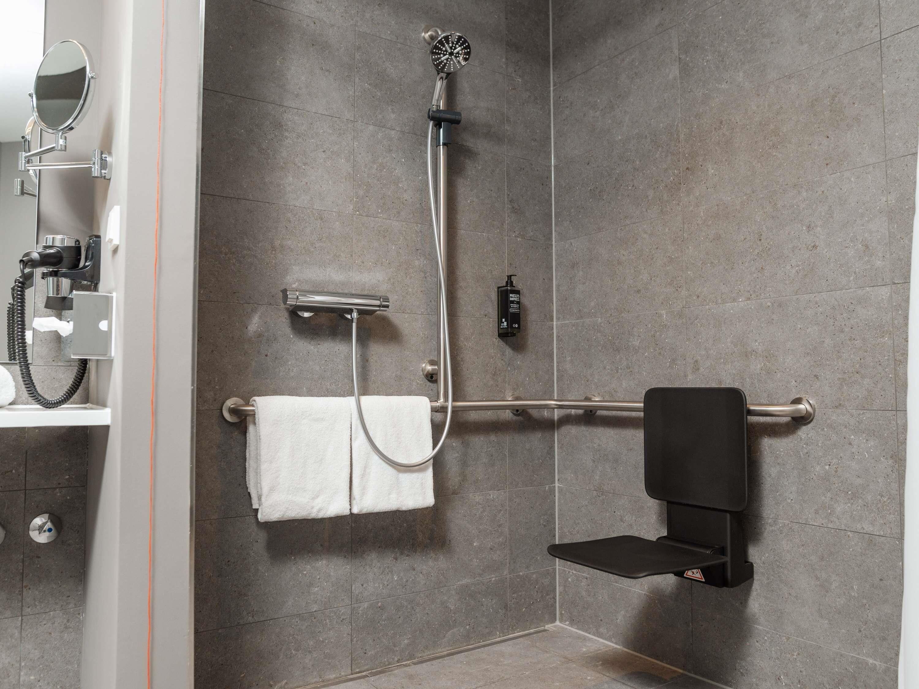 A shower with a handheld showerhead, a towel rack, and a soap dispenser.