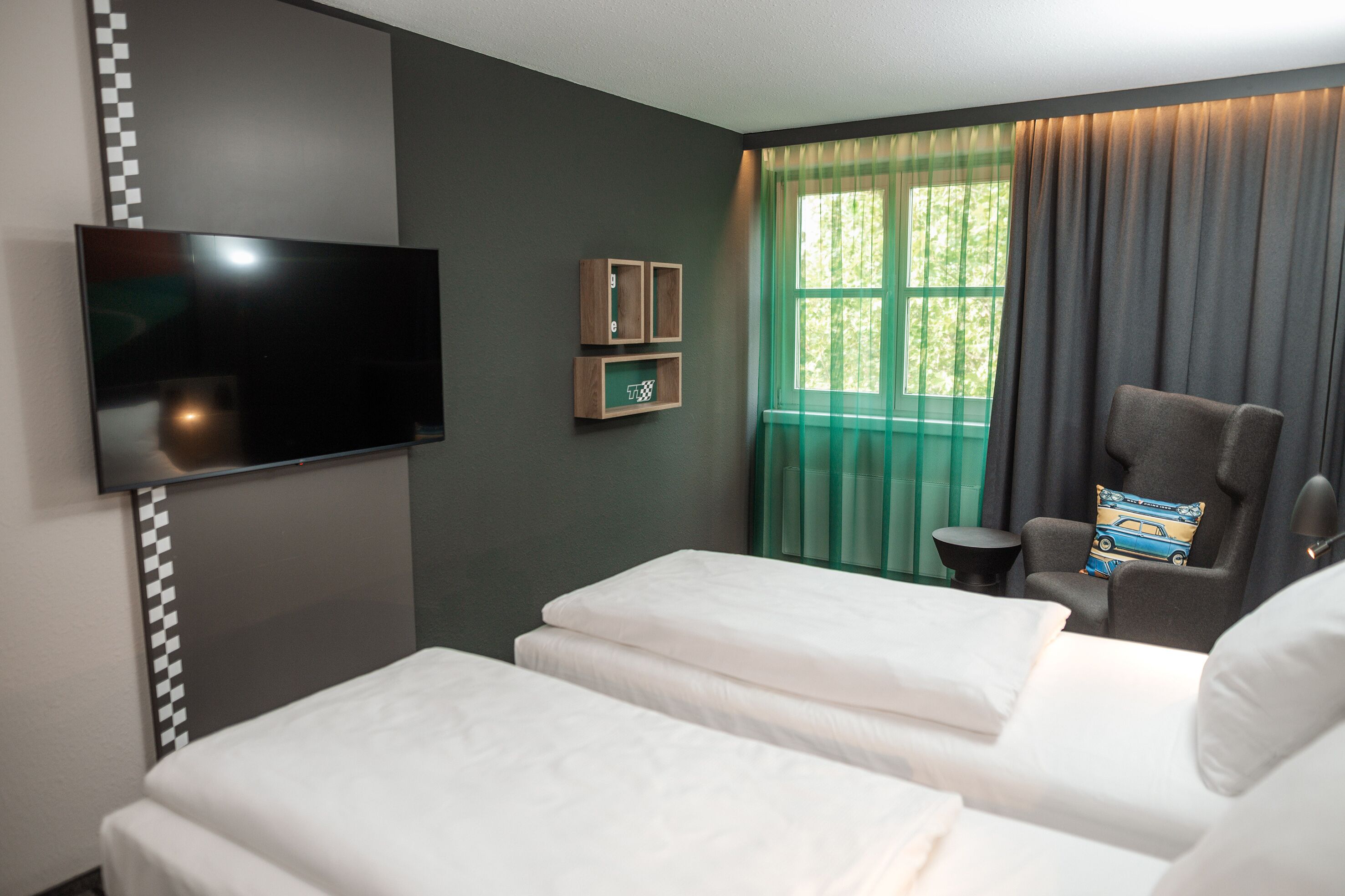 Ein Hotelzimmer mit zwei Betten, einem Flachbildfernseher, einem kleinen Tisch und einem Fenster mit Vorhängen.