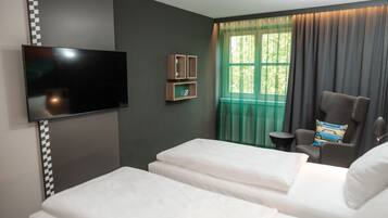 Ein Hotelzimmer mit zwei Betten, einem Flachbildfernseher, einem kleinen Tisch und einem Fenster mit Vorhängen.