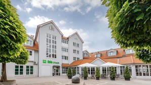 A courtyard with a paved area, a stone sculpture, and a building with a white facade and red roof tiles. - ibis Styles Neckarsulm  (Neckarsulm)