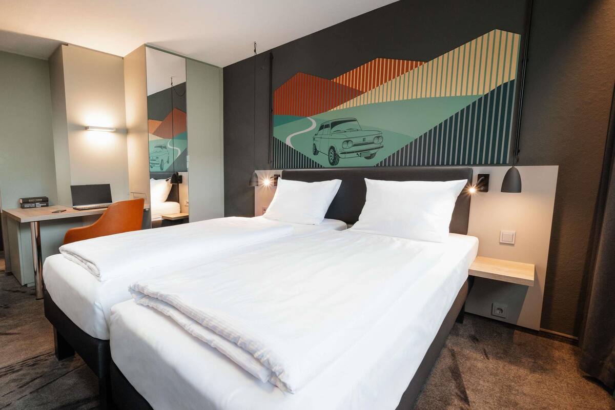 A hotel room with a large bed, a desk with a laptop, and a chair.