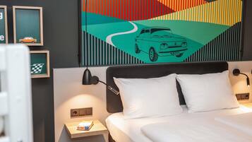Habitación de hotel con cama, dos mesitas de noche, una lámpara de pared y un cuadro abstracto colorido sobre la cama.