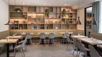 A modern restaurant with wooden shelves, green seating, and pendant lighting.