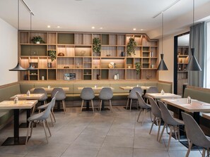 A modern restaurant with wooden shelves, green seating, and pendant lighting. - ibis Styles Neckarsulm  (Neckarsulm)
