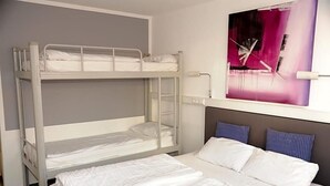 A bunk bed room with a lower bunk, a single bed, and a wall-mounted shelf with a painting.