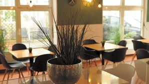 Uma área de refeições com mesas, cadeiras, uma planta em vaso e luminárias pendentes.