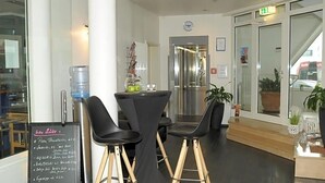 A modern interior with a reception desk, black chairs, a water dispenser, and a chalkboard menu.