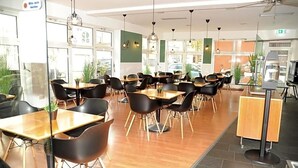 A modern dining area with wooden tables and black chairs, large windows, and ceiling fans.