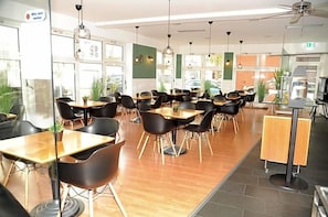 Un comedor moderno con mesas de madera y sillas negras, ventanas amplias y ventiladores de techo.