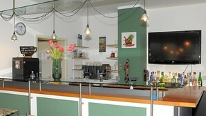 A bar area with a glass counter, chairs, a clock, a coffee machine, a TV, and various bottles.