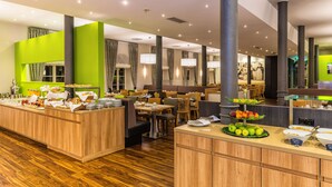 A hotel lobby with a buffet area, wooden flooring, and a green accent wall.