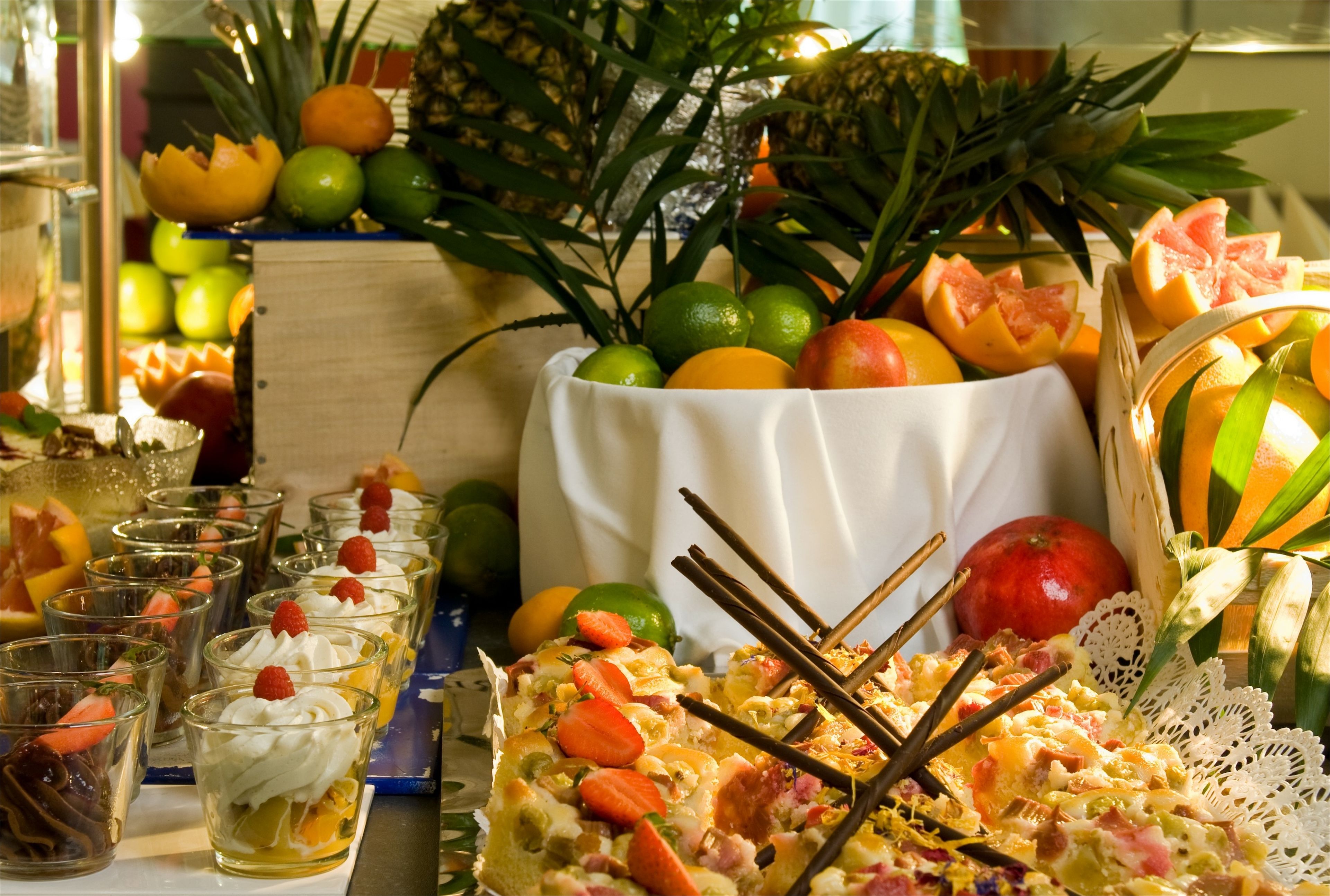 A table with various fruits, a white bowl, and glasses of a layered dessert.