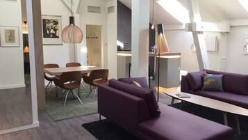 A modern living room with a purple sofa, a dining area with a wooden table and chairs, and a kitchen in the background.