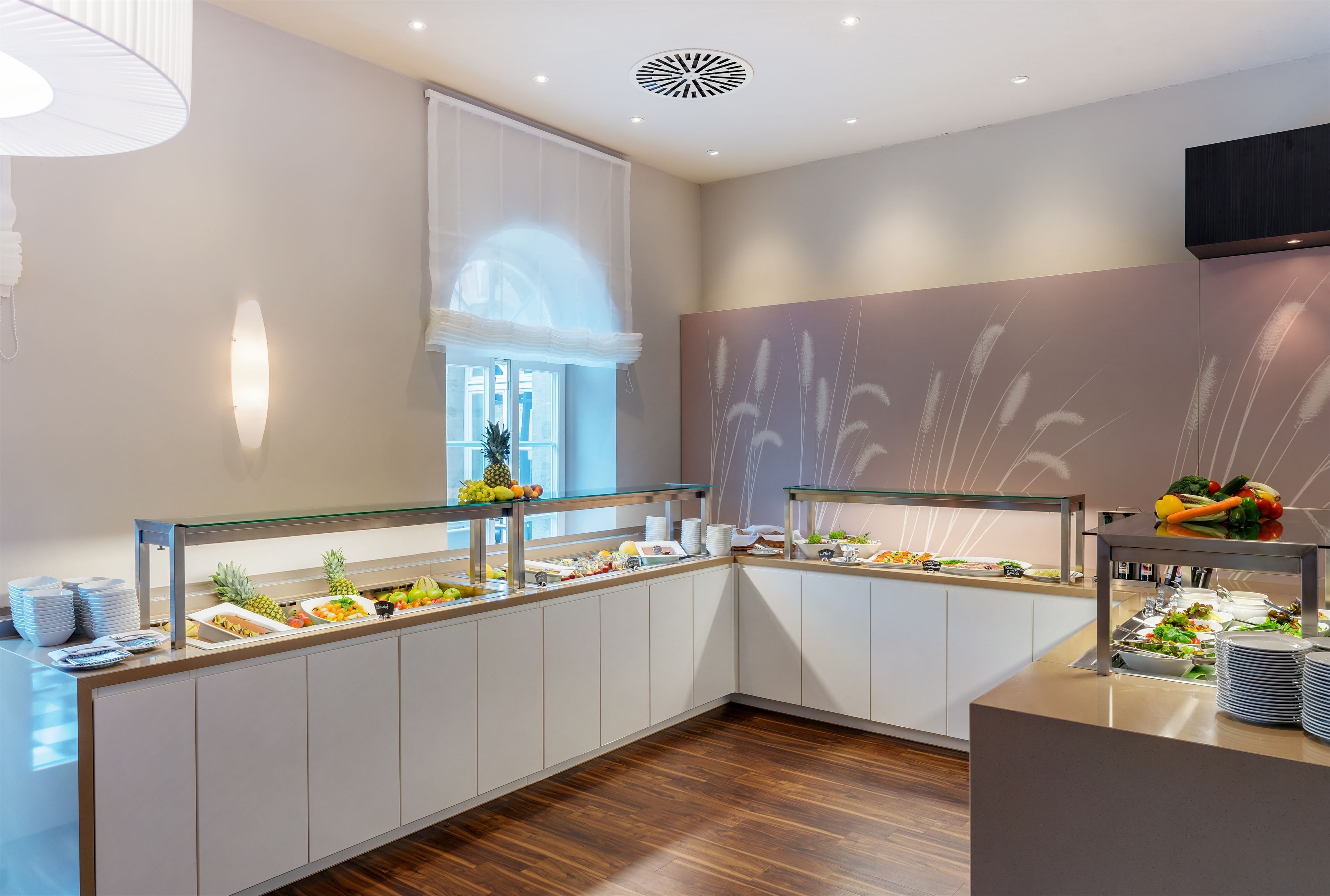 Une cuisine moderne dotée d’une cloison en verre, de meubles en bois et d’une variété d’aliments exposés sur le comptoir.