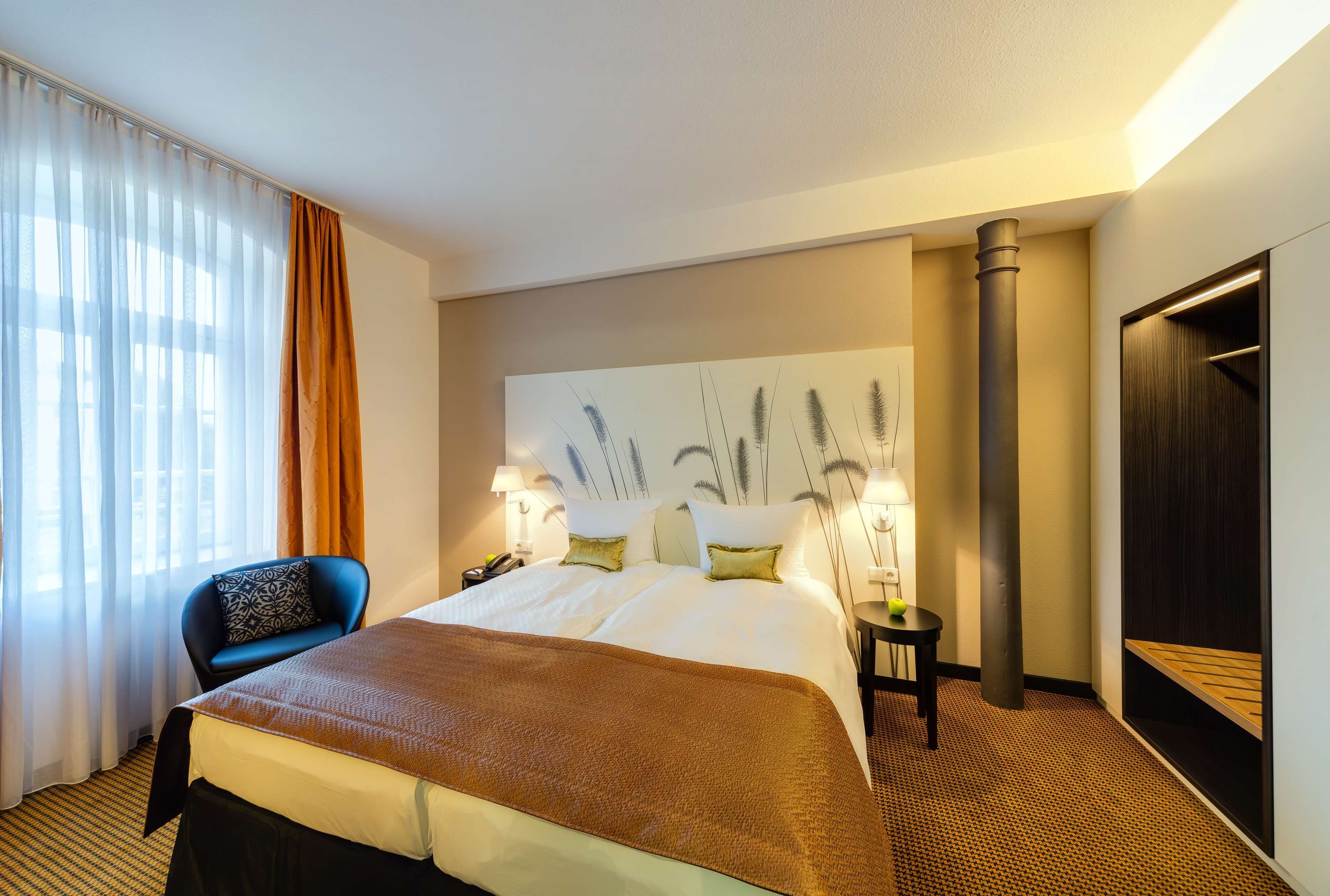 Una habitación de hotel con una cama grande, una silla, una mesita de noche, una lámpara y un armario.