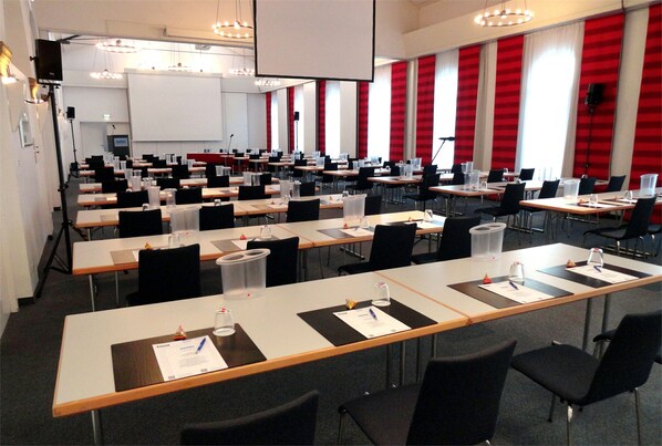A conference room with multiple tables, chairs, and a large screen.