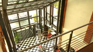 A high-ceilinged lobby with a checkered floor, large windows, and a metal railing.