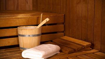A wooden sauna with benches, a wooden bucket with a ladle, and a folded towel.