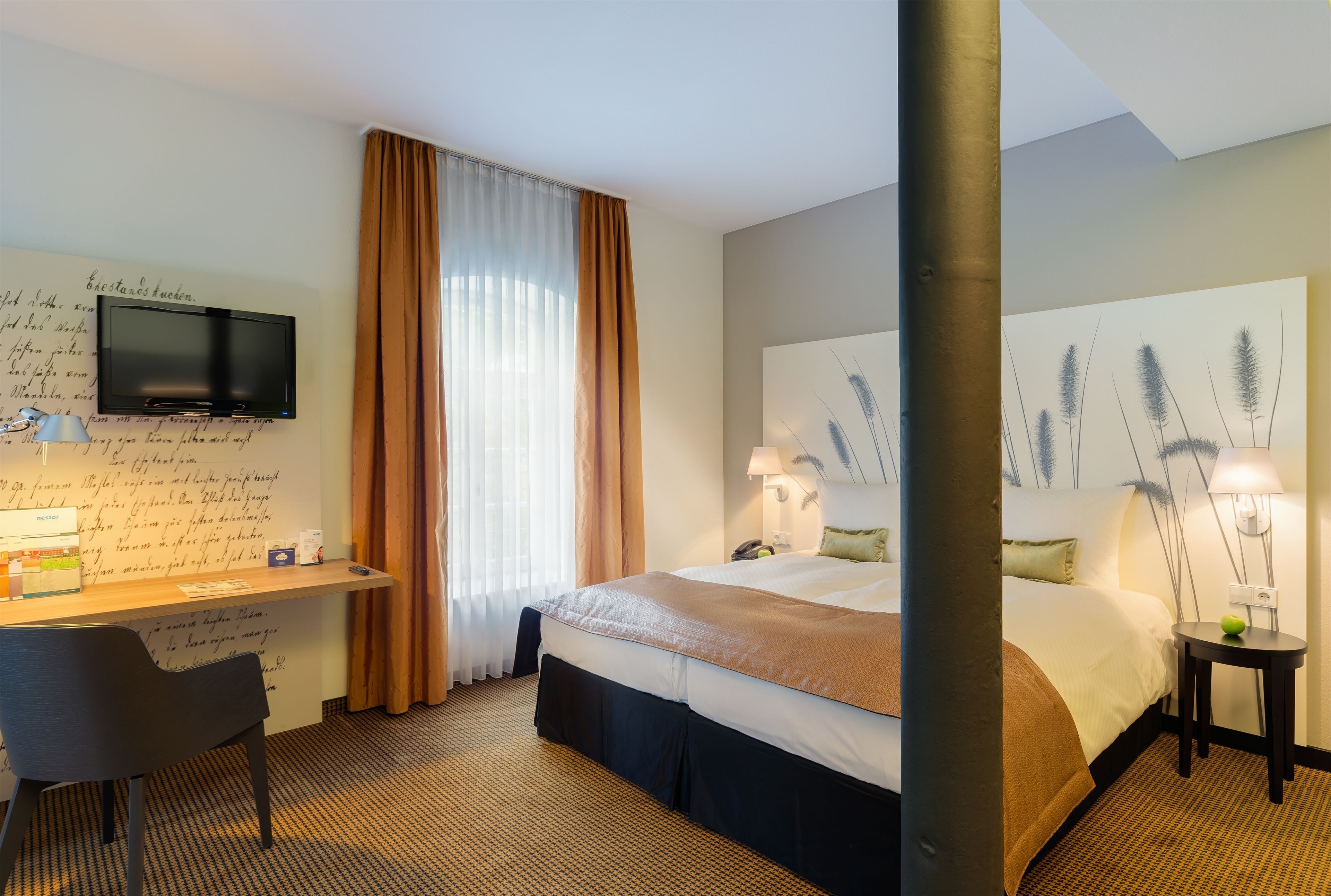 A hotel room with a bed, a desk, a television, and a large window with curtains.